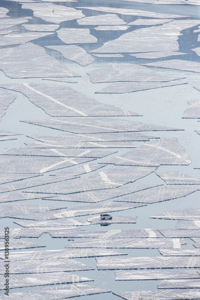 Aerial view of a car floating on an ice floe in the sea. Emergency situation. Ice began to split and crack in a sea bay. Fishermen's car was carried out to sea on a broken ice floe. Spring ice drift.