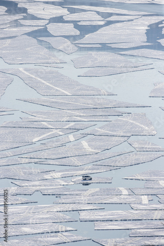 Aerial view of a car floating on an ice floe in the sea. Emergency situation. Ice began to split and crack in a sea bay. Fishermen's car was carried out to sea on a broken ice floe. Spring ice drift.