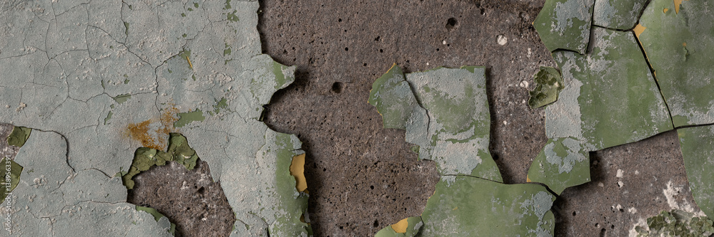 Peeling paint on the wall. Panorama of a concrete wall with old cracked flaking paint. Weathered rough painted surface with patterns of cracks and peeling. Wide panoramic grunge texture for background