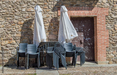 set of chairs, table and folded umbrellas next to a door and a brick wall