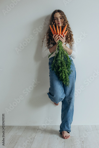 Portrait of smiling beautiful girl showing carrot on white background