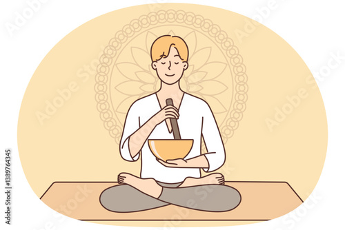 Meditating man sitting in lotus position on yoga mat using bowl to perform ancient ritual