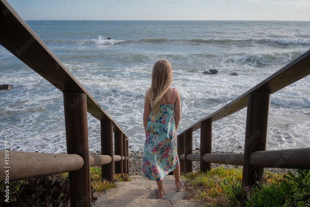 Beautiful blonde girl in a long dress walks along the sea coast