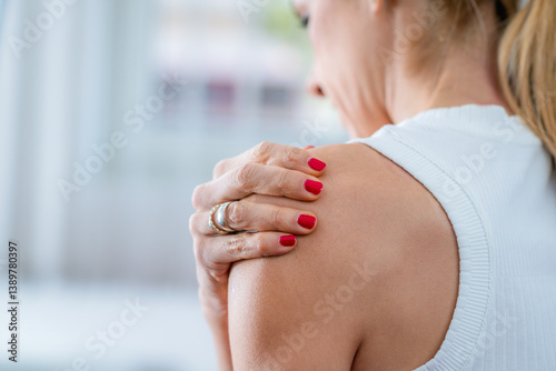 A woman experiencing shoulder pain, touching her sore muscles with discomfort. The image highlights tension, muscle strain, or possible injury, often caused by poor posture, stress, or overuse.