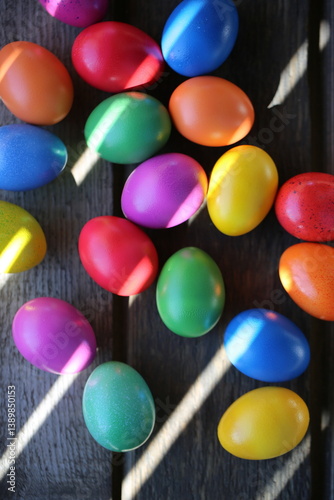 The Easter colorful eggs are lying on the wooden table. Sunrays are breaking through the wooden fence.