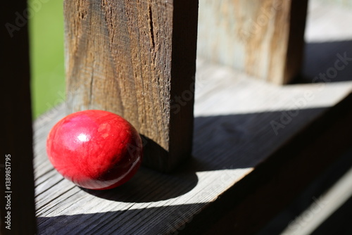 A red egg is lying on the wooden balcony between the railing bars. A red egg is lying on the wooden balcony between the railing bars.