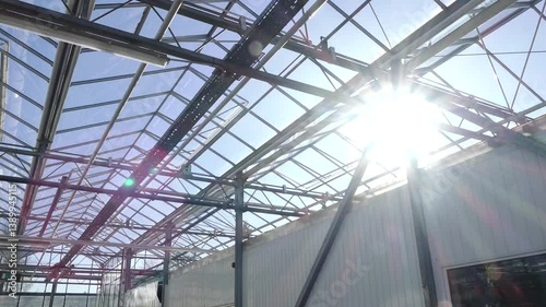 Modern greenhouse interior featuring rows of hanging orange pots connected to an automated irrigation system, under a glass roof with natural sunlight.