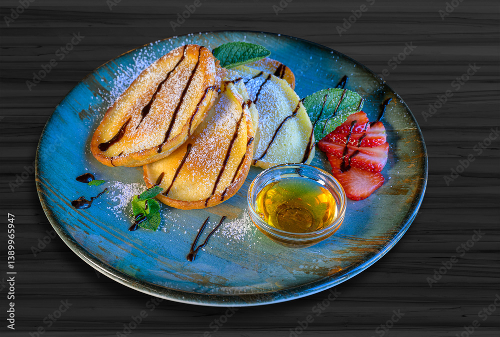sweet pancakes with syrup, powdered sugar, honey and strawberries served on a blue plate