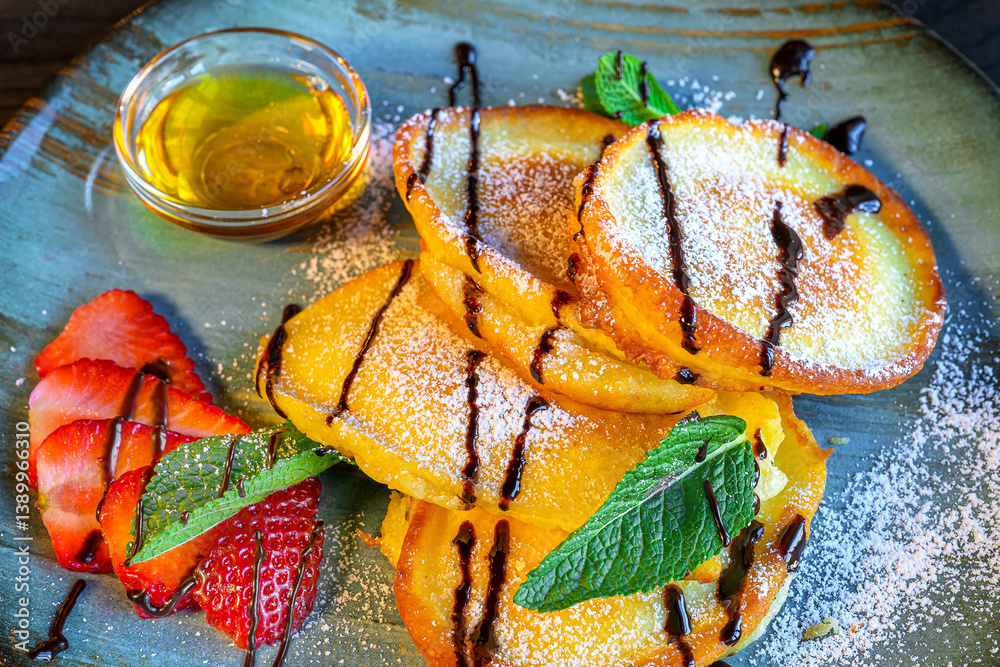 sweet pancakes with syrup, powdered sugar, honey and strawberries served on a blue plate