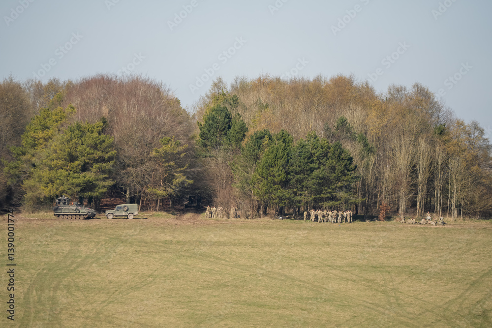 British army soldiers and with an FV512 Warrior and Wolf utility vehicle gathered by woodland