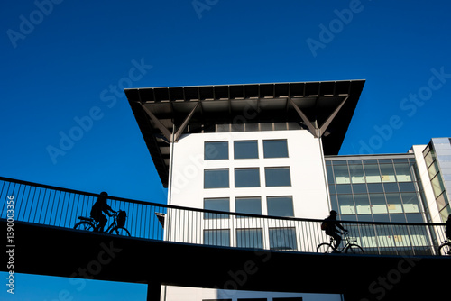 Urban cyclist crossing footbridge with architecture in Copenhagen, Denmark, showcasing ecological commuting, smart city planning and modern city life solutions.