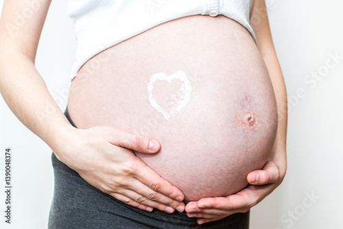 Heart made of moisturizing cream on pregnant belly