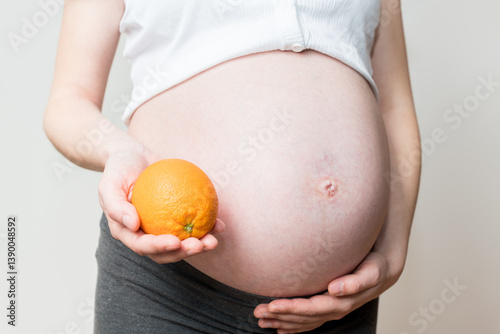 natural vitamins for pregnant women, fruits during pregnancy, orange in hand and pregnant belly