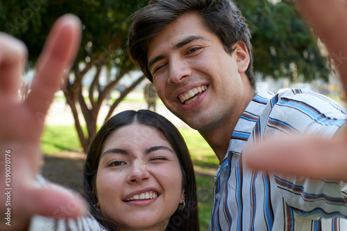 Smiling young couple in a park, playfully posing for a selfie, capturing a candid moment