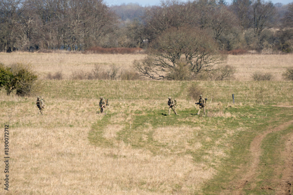 British army infantry soldiers moving moving across a meadow in early spring in sunshine