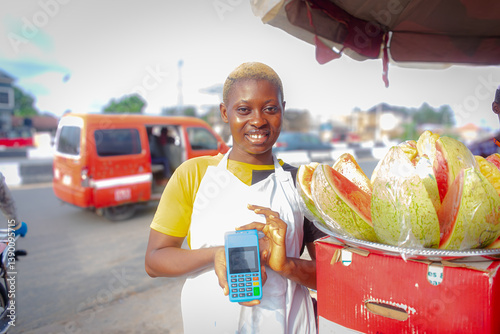 Happy African fruit seller standing holding a pos machine wearing white apron