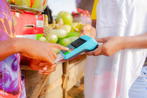 Person paying for fruits with a credit card while african fruit seller woman holding an electronic POS machine