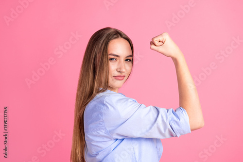 Confident young woman showing strength with flexed arm on pink background, representing empowerment, determination, and self-confidence