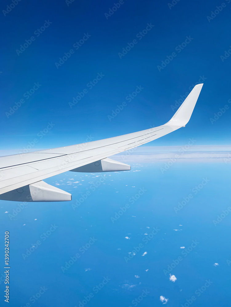 Obraz premium Flying above the ocean - window seat view. White airplane wing against clean blue sky at the height of 10 000 meters.