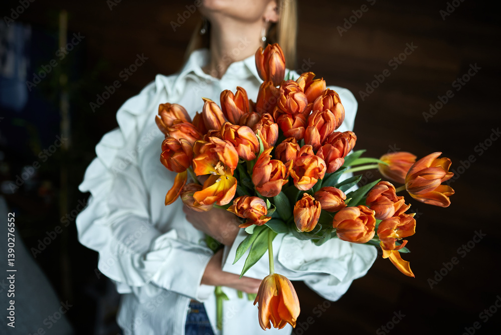 Elegant woman holding vibrant orange tulips bouquet in bright room, symbolizing freshness and beauty, floral arrangement concept