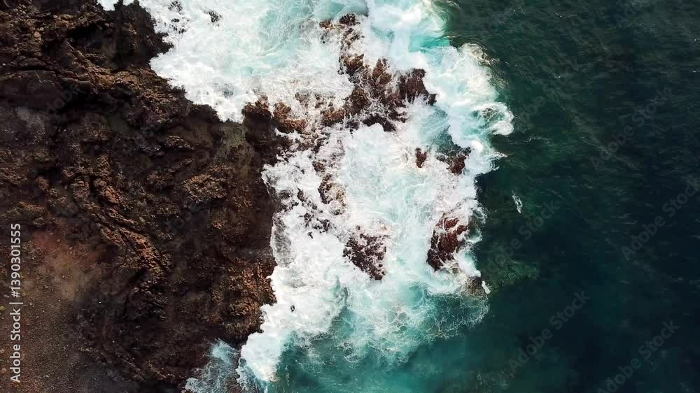 Drone view of Atlantic ocean waves meet with underwater pointed rocky. Blue rough sea with big waves with foam crashing against the rocks, south of Tenerife, Canary island