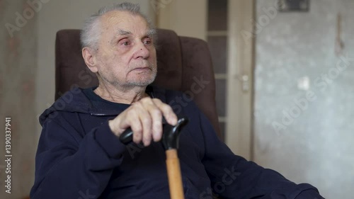 Elderly Man Holding Cane Sitting in Armchair Indoors