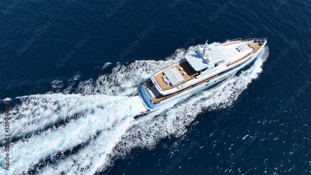 Aerial drone tracking photo of beautiful modern super yacht with wooden deck cruising in low speed deep blue Mediterranean sea