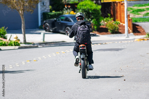 Rear view of a cyclist wearing a helmet and backpack on an e-bike traveling along a residential road
