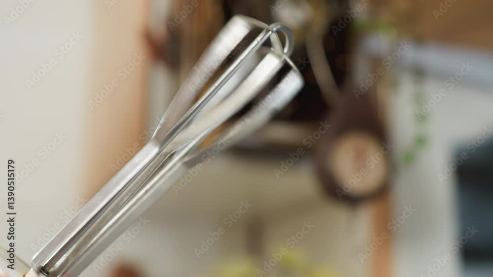 Close up of electric mixer whisk attachment rotating rapidly during mixing process in kitchen setting, showing motion blur from speed with soft background of utensils Close up of electric mixer whisk attachment rotating rapidly during mixing process in kitchen setting, showing motion blur from speed with soft background of utensils