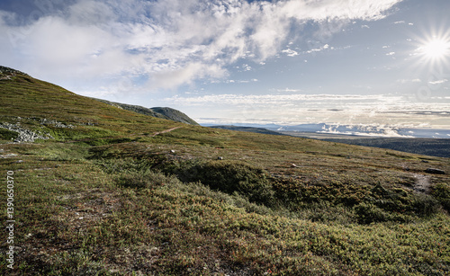 Morning in Idre Dalarna reveals a vast serene Nordic landscape, with soft light casting shadows on the verdant hills and distant mountains. A peaceful atmosphere fills the air