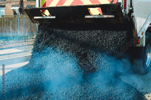 Hot asphalt dumped from delivery truck onto construction site for road repair and maintenance work 