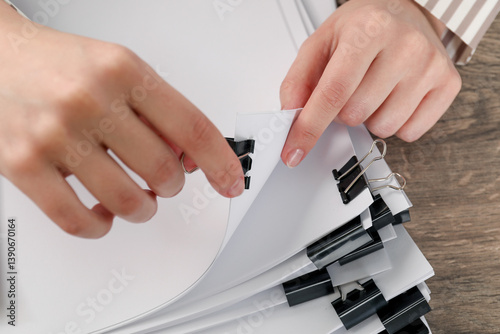Woman attaching sheets of paper with metal binder clip at table, closeup