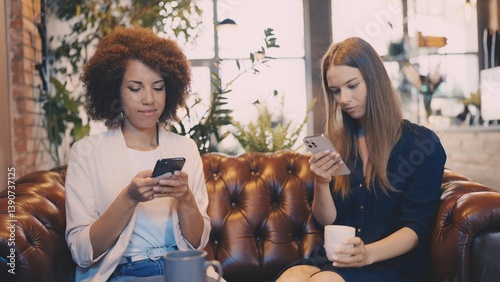 Two friends scrolling on their phones in cafe, disconnected in social setting