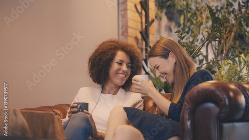 Two female friends sharing sincere laughter and enjoying coffee in cozy coffeehouse
