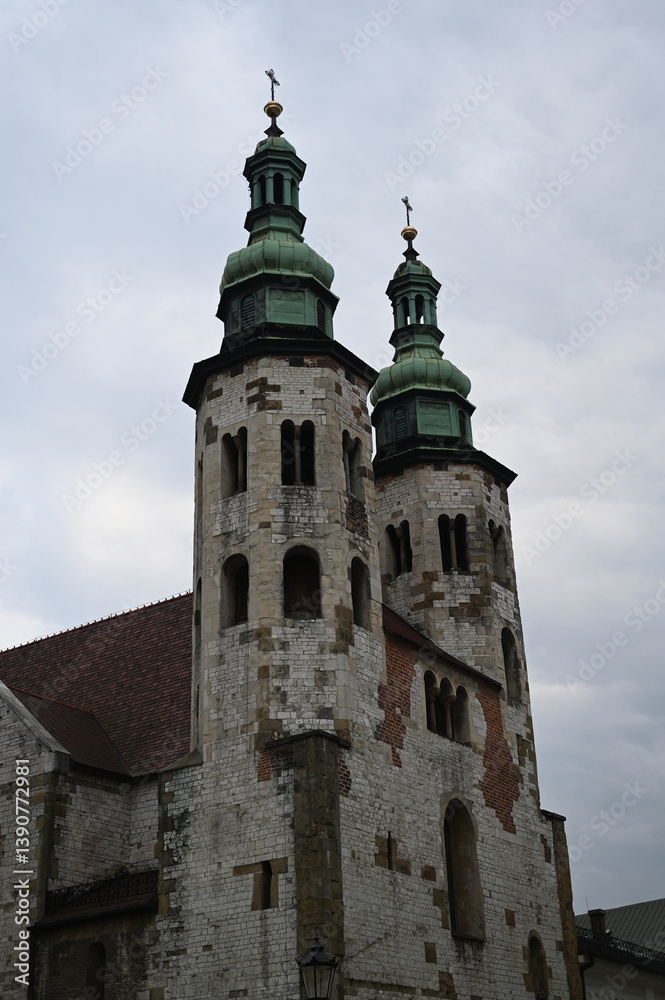 Fototapeta premium Historic tower with spire against dramatic cloudy sky. Old European architecture with gothic details and red brick wall