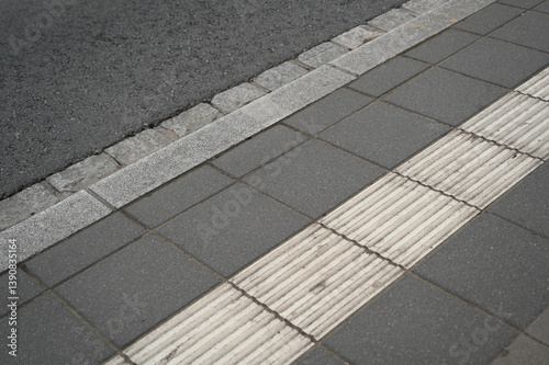 sidewalk with tactile paving, grey tiles, and a stone curb next to the asphalt road. Urban infrastructure detail illustrating accessibility, pedestrian safety, and modern city design.