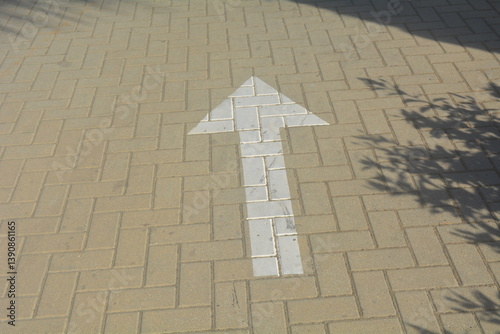 Directional arrow painted on pavement guiding foot traffic in a sunny outdoor area
