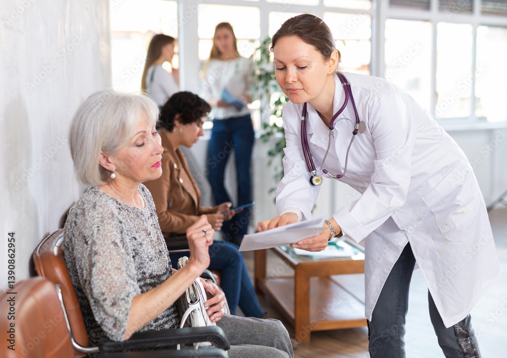 Obraz premium Polite qualified female doctor in white coat showing results of medical examination and explaining prescribed treatment to worried interested senior woman sitting in clinic lobby