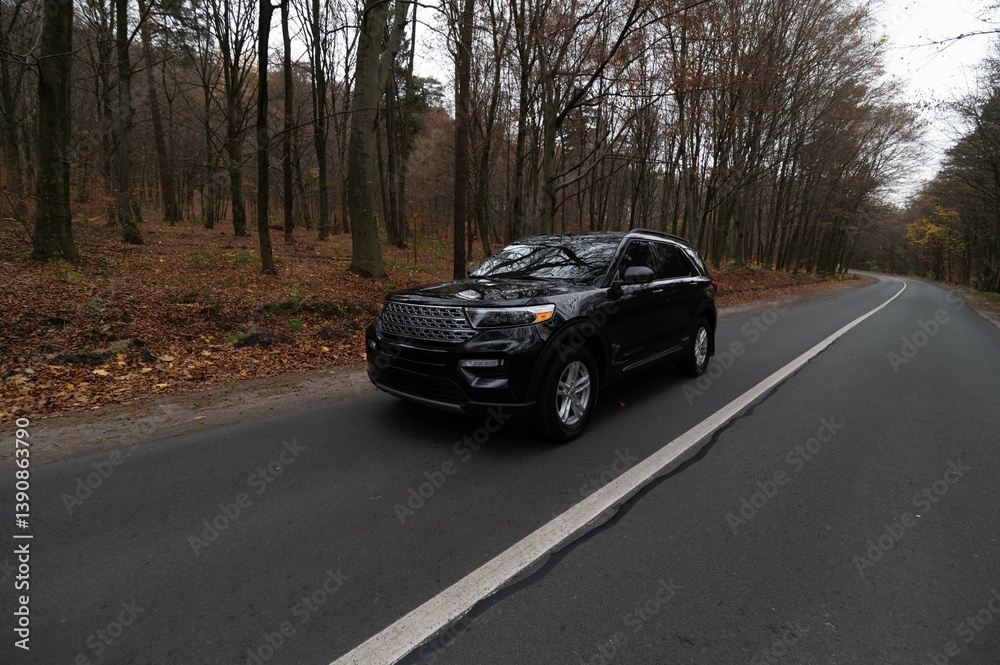 A black SUV cruising along a picturesque road surrounded by autumn foliage in a serene forest setting. A black SUV cruising along a picturesque road surrounded by autumn foliage in a serene forest setting.
