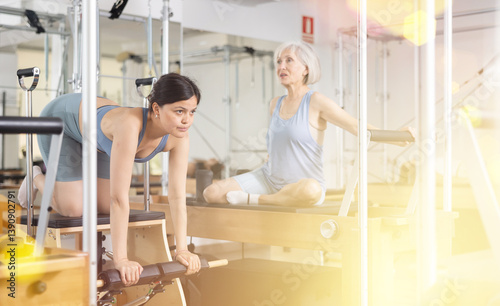 Interested focused young asian girl doing remedial gymnastic in pilates studio, exercising on wunda chair.. photo