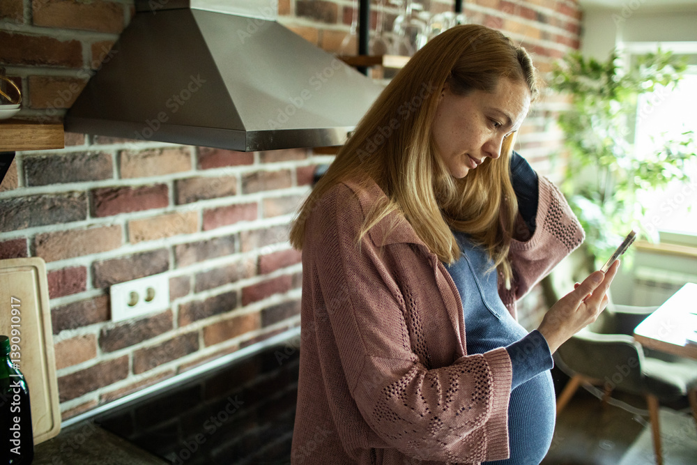 Smiling pregnant woman using smartphone at home in modern kitchen