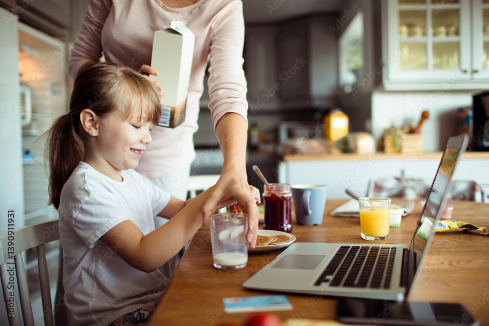 Single mother and daughter having breakfast together in the morning while using a laptop in the kitchen Single mother and daughter having breakfast together in the morning while using a laptop in the kitchen