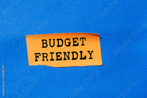 Budget friendly message written on ripped torn orange paper on blue background. Conceptual budget friendly symbol. Copy space. photo