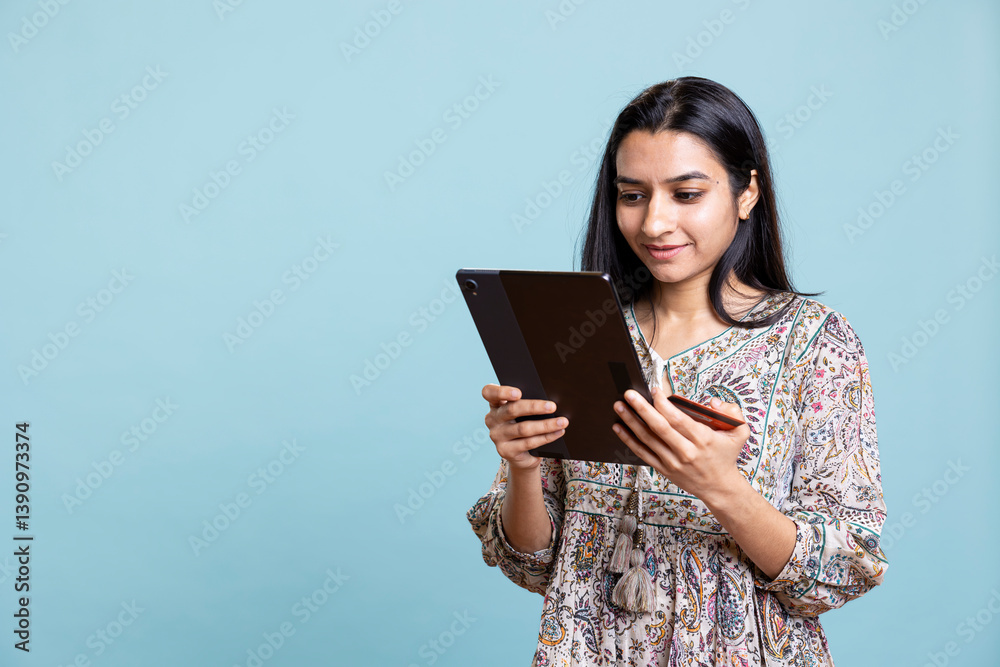 Indian person excited to purchase stuff adding payment method on website with her tablet, isolated over studio background. Ecstatic client does internet shopping, typing debit card info. Indian person excited to purchase stuff adding payment method on website with her tablet, isolated over studio background. Ecstatic client does internet shopping, typing debit card info.