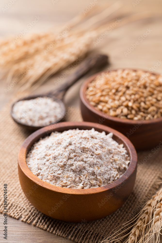 Whole wheat flour with wheat grain in bowl on wooden background Whole wheat flour with wheat grain in bowl on wooden background