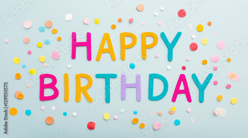 Happy birthday message made of colorful felt letters with scattered confetti on light blue background for festive greeting and celebration design