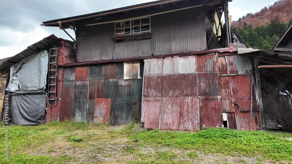 Dilapidated and patched building with corrugated iron walls and roof, showing signs of decay and disrepair in the rural landscape of Shirakawa go Village