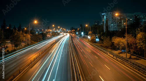 Night time long exposure shot of highway with car light trails and city buildings in the distance