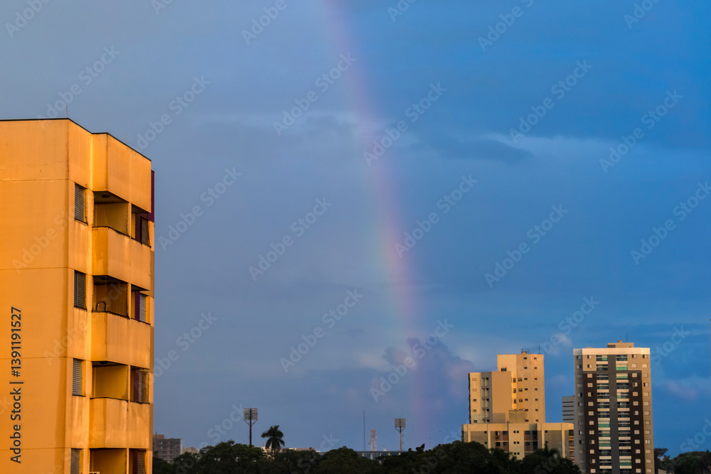 Rainbow over cityscape. Urban buildings under a colorful arc in the sky. Serene scene, perfect for illustrating city life and weather phenomena