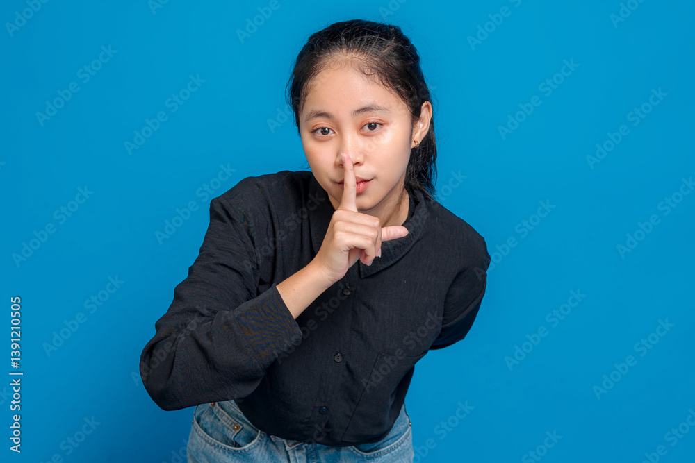 Young woman with serious expression making quiet gesture by placing finger on lips, symbolizing silence or secrecy, ideal for advertising concepts about privacy or confidentiality. Young woman with serious expression making quiet gesture by placing finger on lips, symbolizing silence or secrecy, ideal for advertising concepts about privacy or confidentiality.